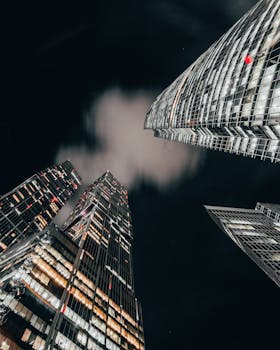 A dramatic upward view of illuminated skyscrapers against a night sky.