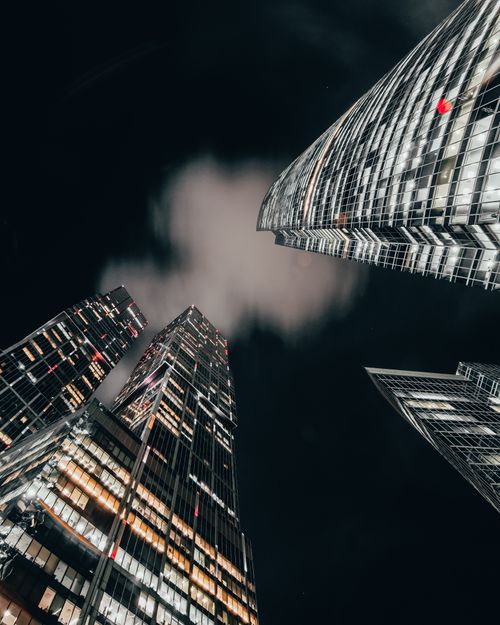 Free A dramatic upward view of illuminated skyscrapers against a night sky. Stock Photo