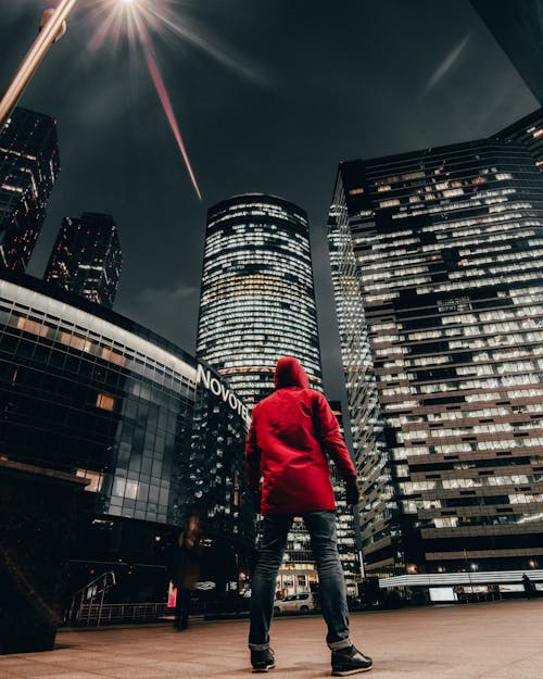 Person in Red Hoodie Jacket Standing in Front of High Rise Buildings