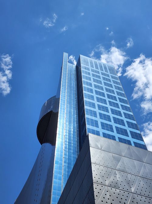 Free Low angle view of a sleek glass skyscraper with a clear blue sky background. Stock Photo