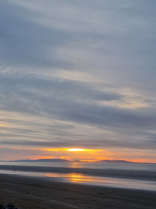 Free A breathtaking view of the sun setting over a calm ocean, casting warm hues on the clouds and distant islands. Stock Photo