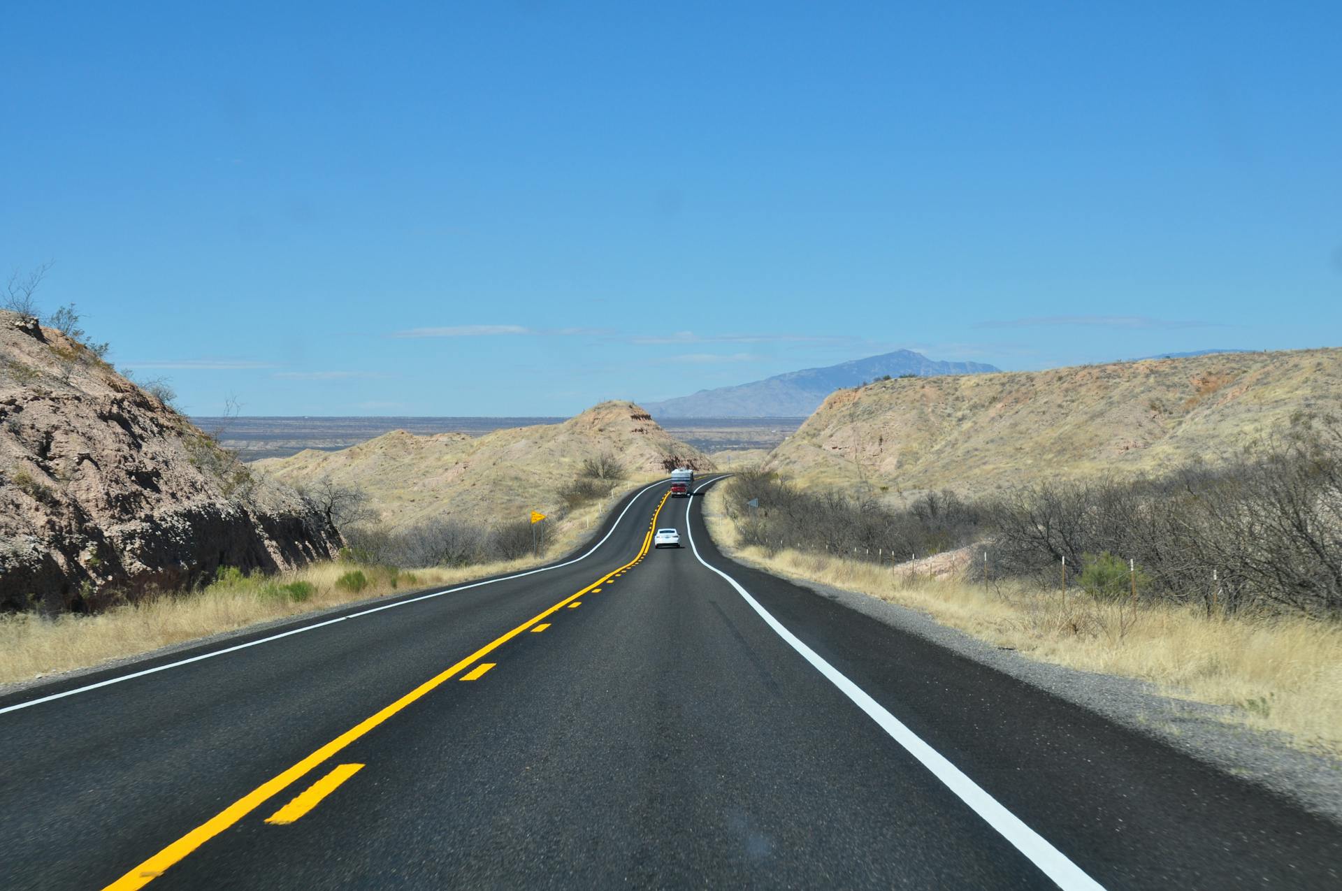 A tranquil desert highway in Arizona stretches towards distant mountains under a clear blue sky.