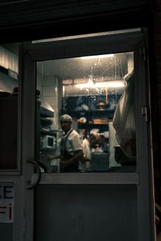 View of chefs in a busy restaurant kitchen through an illuminated door at night.