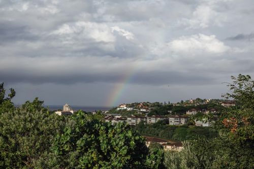 Free Beautiful coastal village landscape with a vibrant rainbow and lush greenery under dark clouds. Stock Photo