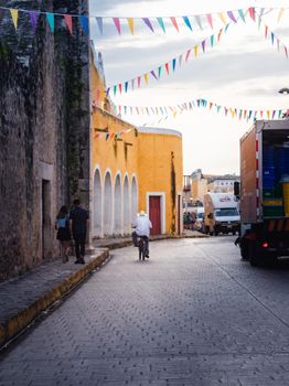 Colorful Mexican street scene with banderitas, people and trucks in a historic town setting.