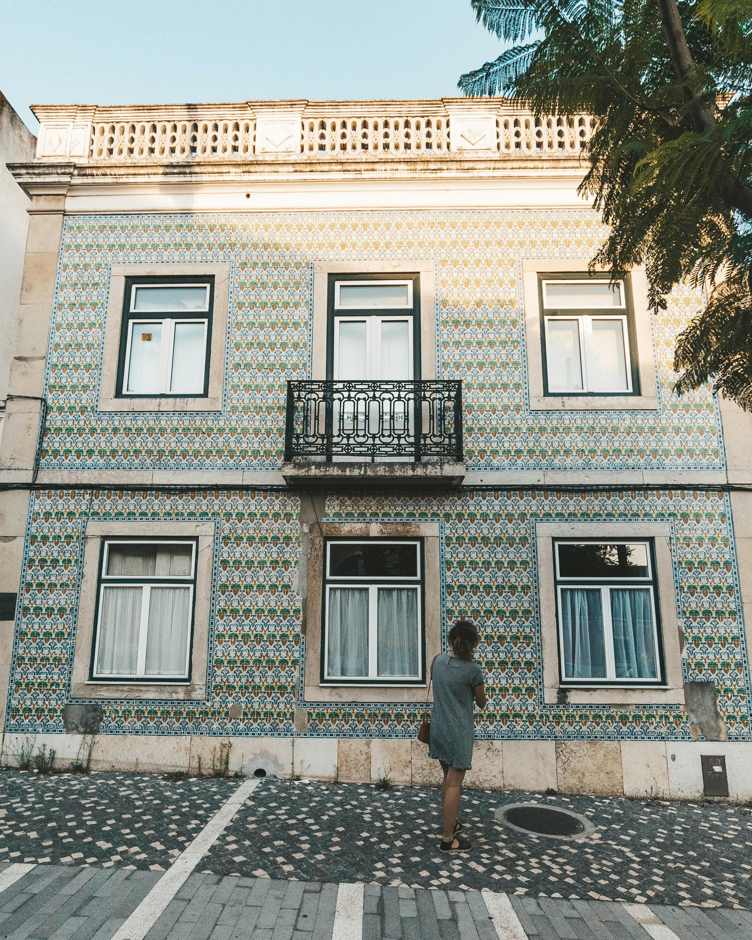 Free Girl in Grey Dress Looking Up At Rustic Green Building on Cobblestone Street in Belem, Lisbon Portugal Stock Photo