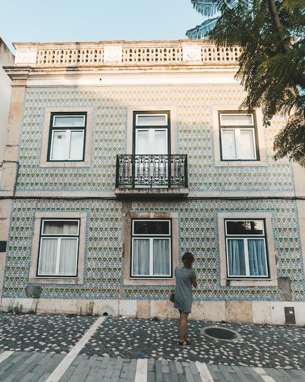 Free Girl in Grey Dress Looking Up At Rustic Green Building on Cobblestone Street in Belem, Lisbon Portugal Stock Photo