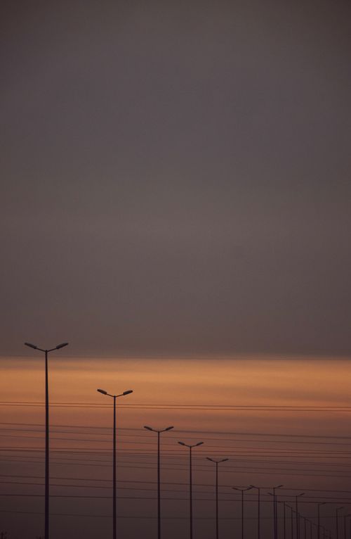 Free A row of street lights silhouetted against a dramatic sunset sky, creating a serene urban landscape. Stock Photo
