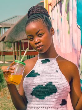 Portrait of a young woman with braids holding a mason jar with a refreshing drink outdoors.