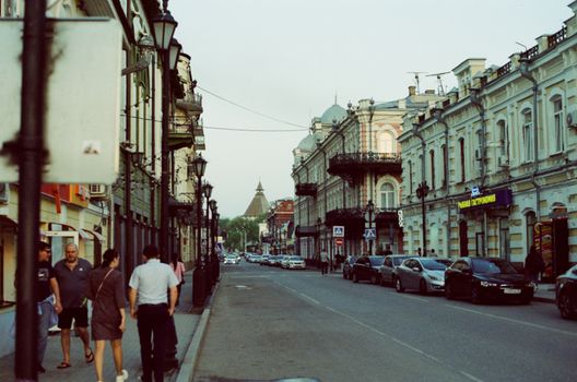 A bustling urban street showcasing historic architecture, pedestrians, and parked cars in a vibrant city.