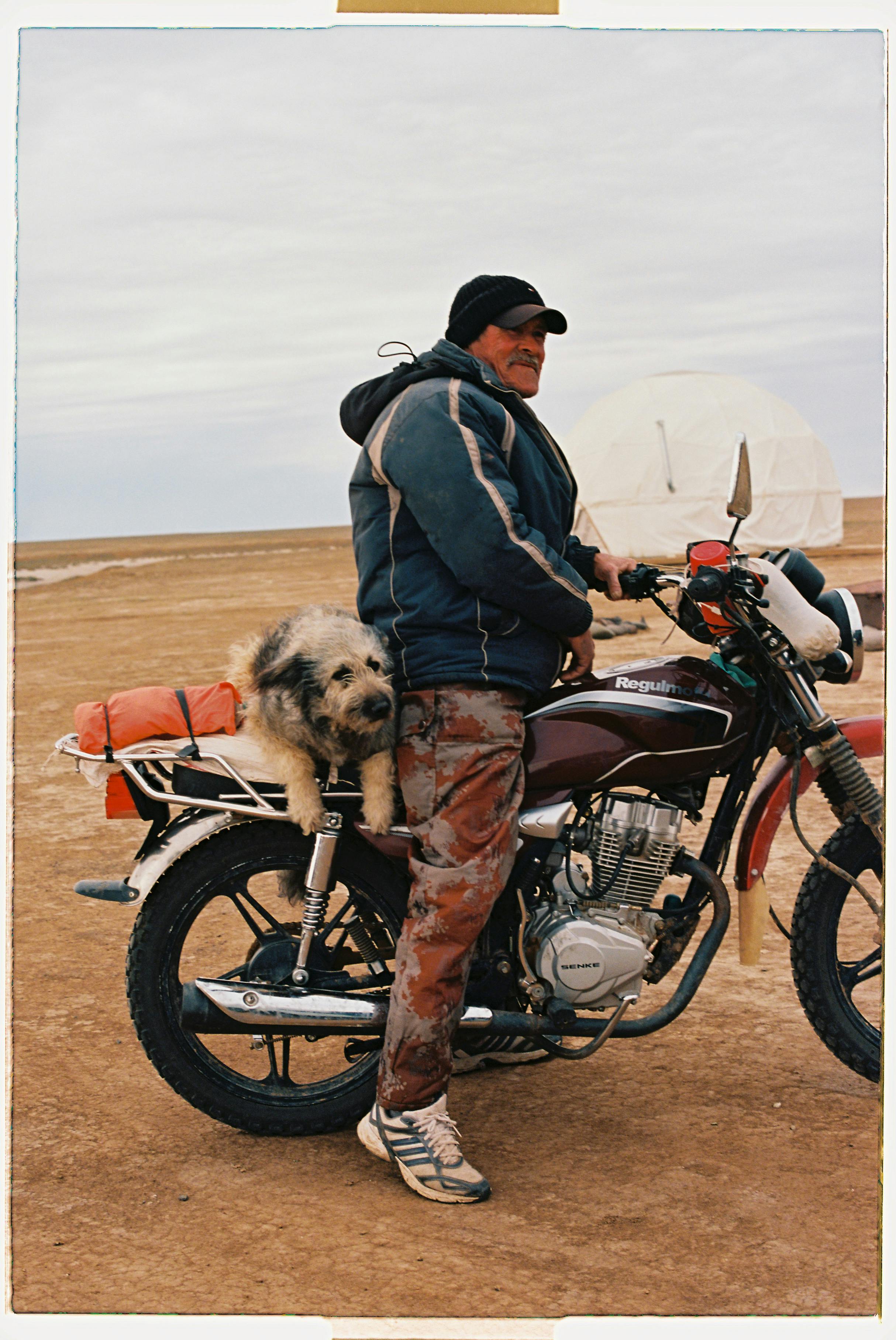 A man with his dog on a motorcycle in a desert landscape, highlighting adventure and travel.