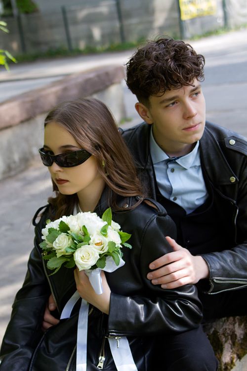 Free A stylish couple in black leather jackets holding a bouquet of white roses outdoors. Stock Photo