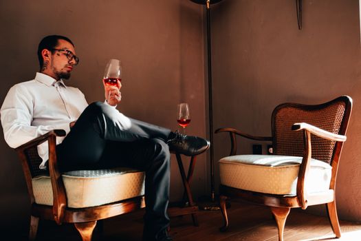 Man in Black Suit Sitting on Chair Holding Wine Glass