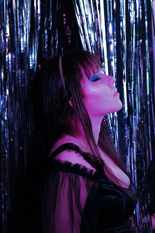 Free Close-up portrait of a woman with blue eyeshadow and closed eyes against a shiny foil curtain. Stock Photo