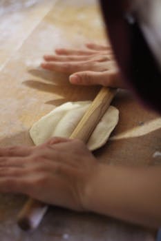 Hands rolling out dough with a wooden pin on a rustic table, highlighting the cooking process.