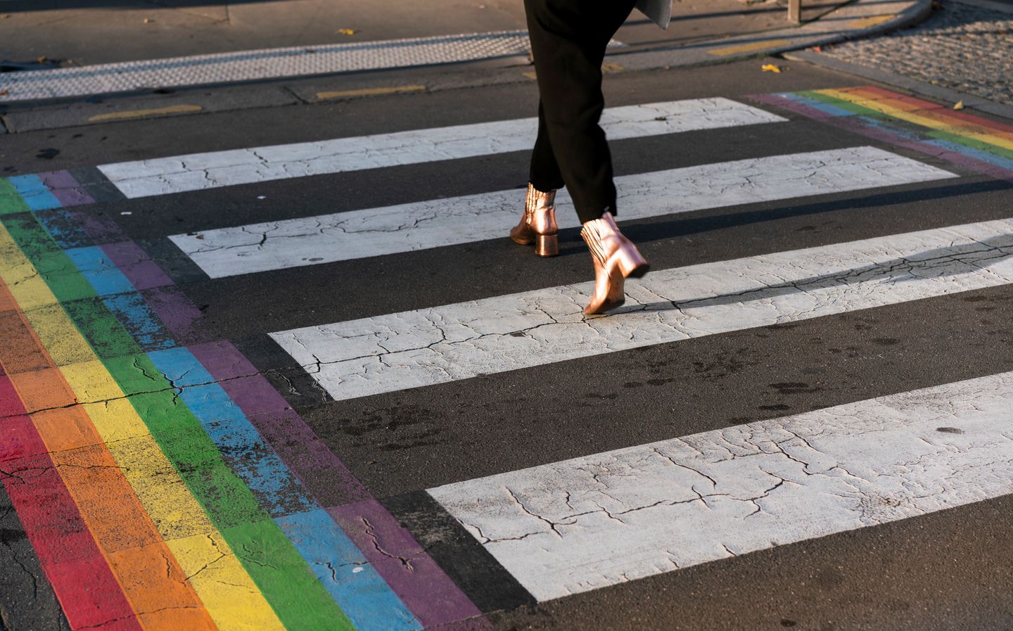 Someone crossing a street at a rainbow crosswalk