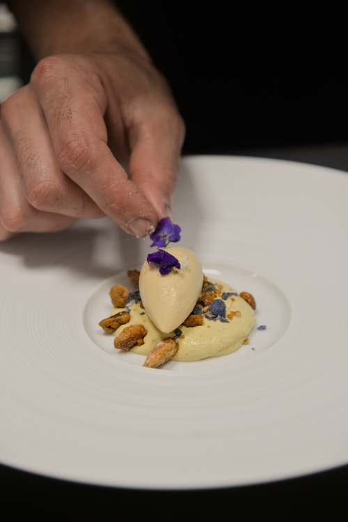 Free Close-up of a chef carefully garnishing a gourmet dessert with edible flowers on a white plate. Stock Photo