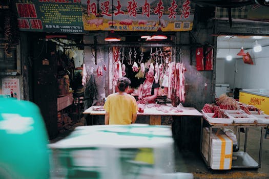 A vibrant scene at a traditional Asian butcher shop with hanging meats and two people interacting.