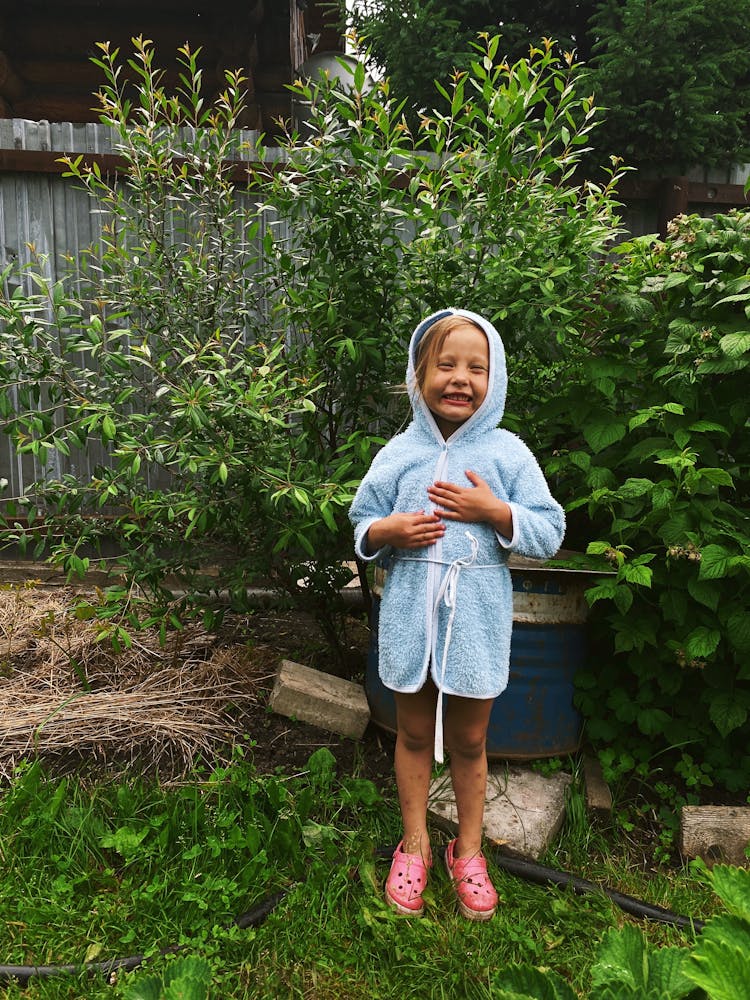 A Young Girl In Blue Hoodie Sweater Standing On Green Grass