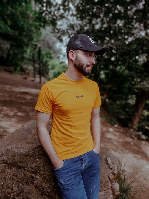 Free Casually dressed man in a yellow shirt leaning on a rock in a forest setting. Stock Photo