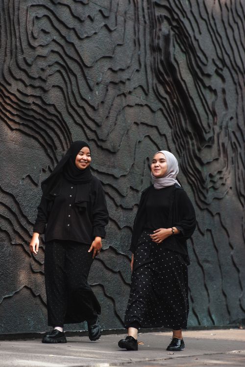 Free Two women in stylish hijabs stroll alongside an artistic textured wall. Stock Photo
