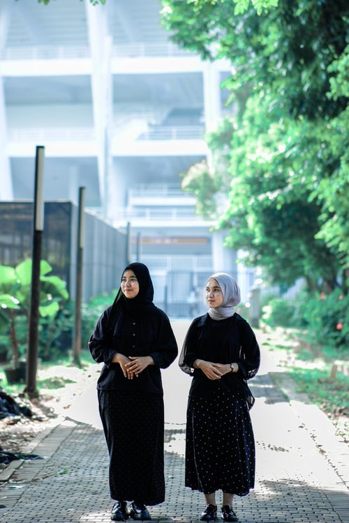 Free Two women in hijabs walk through a lush, urban park setting on a sunny day. Stock Photo