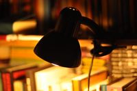 A desk lamp lit over a shelf of books at night — photo by Luke M on Pexels