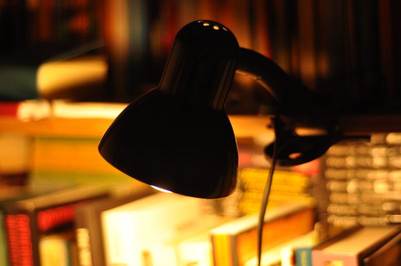 A desk lamp lit over a shelf of books at night — photo by Luke M on Pexels