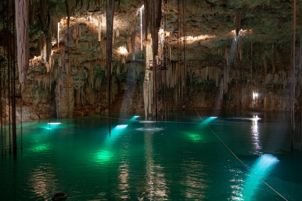 Cenote subterráneo con estalactitas y agua turquesa iluminada desde arriba