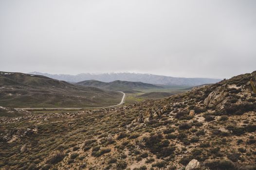 A tranquil mountain road winding through an expansive countryside landscape with rocky terrain.