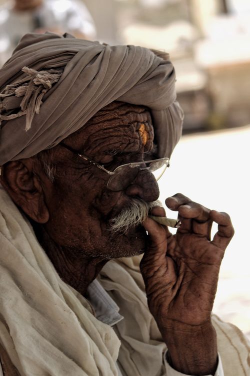 Free Portrait of a senior Indian man with glasses and a turban, smoking outdoors. Stock Photo