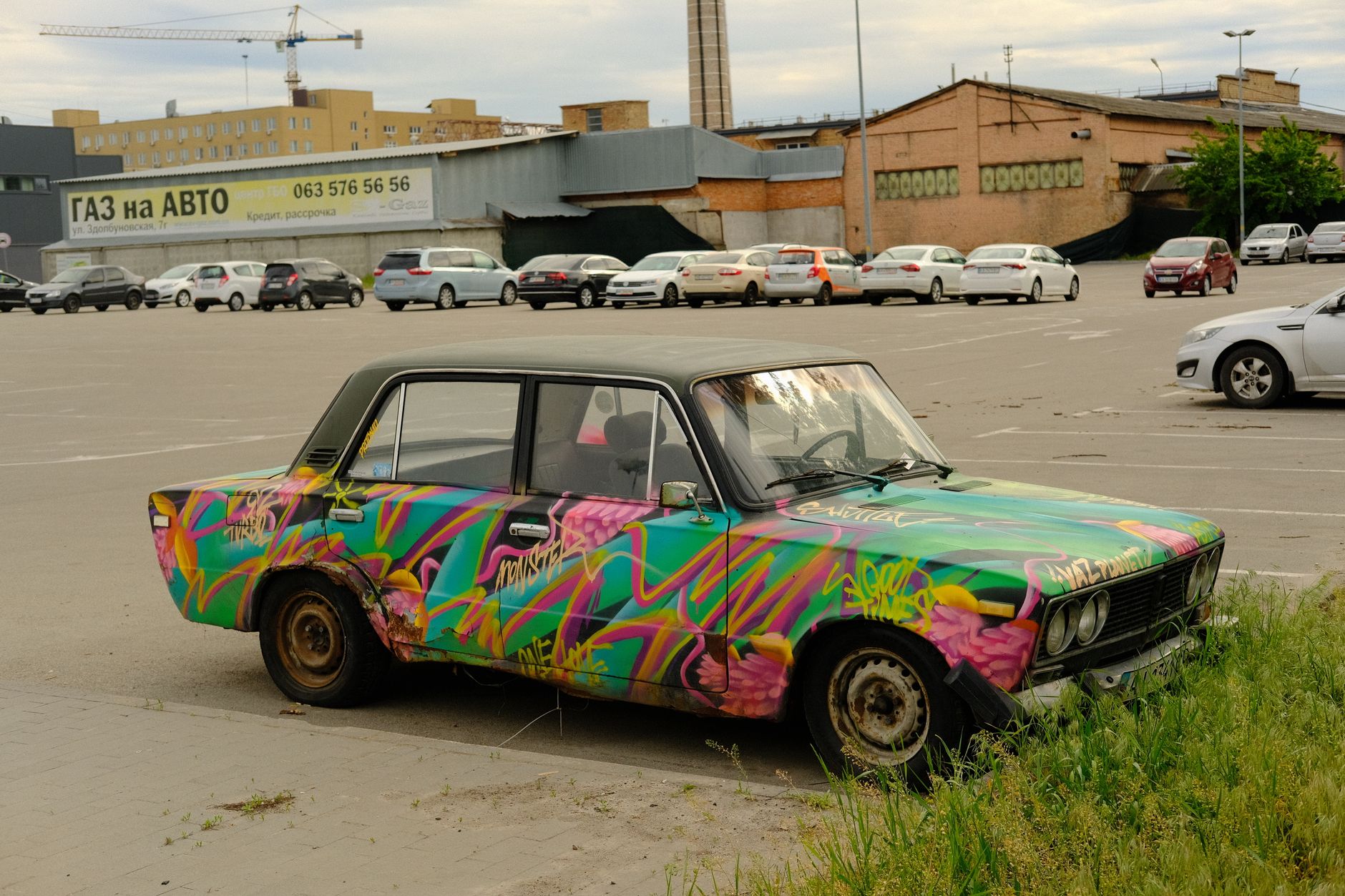 Colorful vintage car with graffiti in a Kyiv parking lot, showcasing urban art culture.