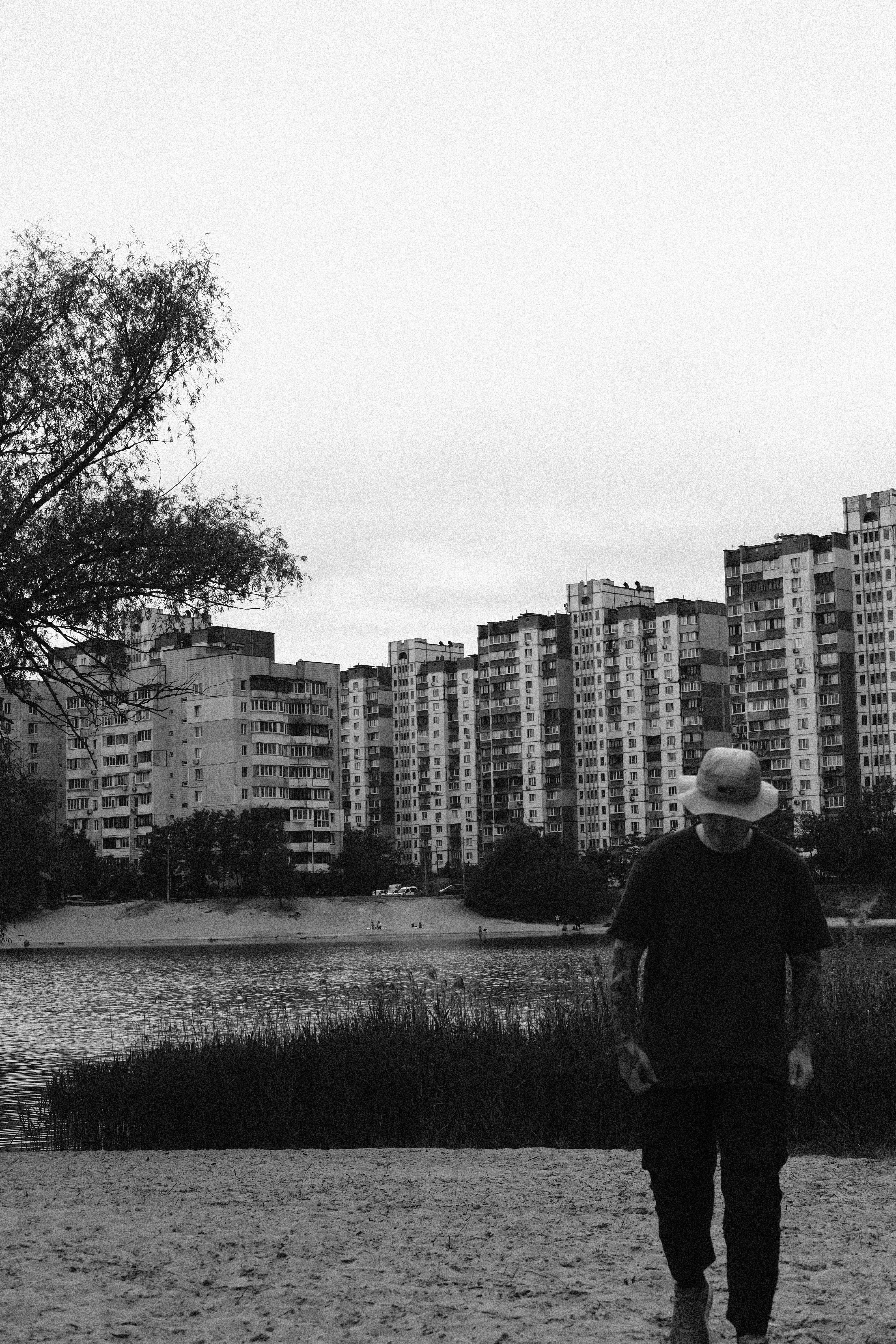 A person walking by the Dnieper River in Kyiv with urban architecture in grayscale.