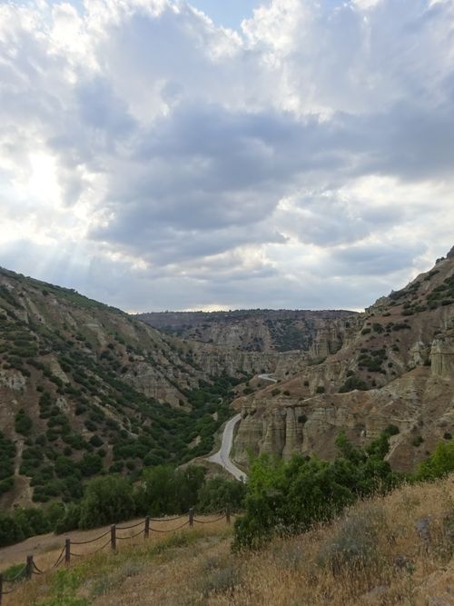 Free Serene valley landscape with hills, a winding road, and dramatic skies. Ideal for nature lovers. Stock Photo