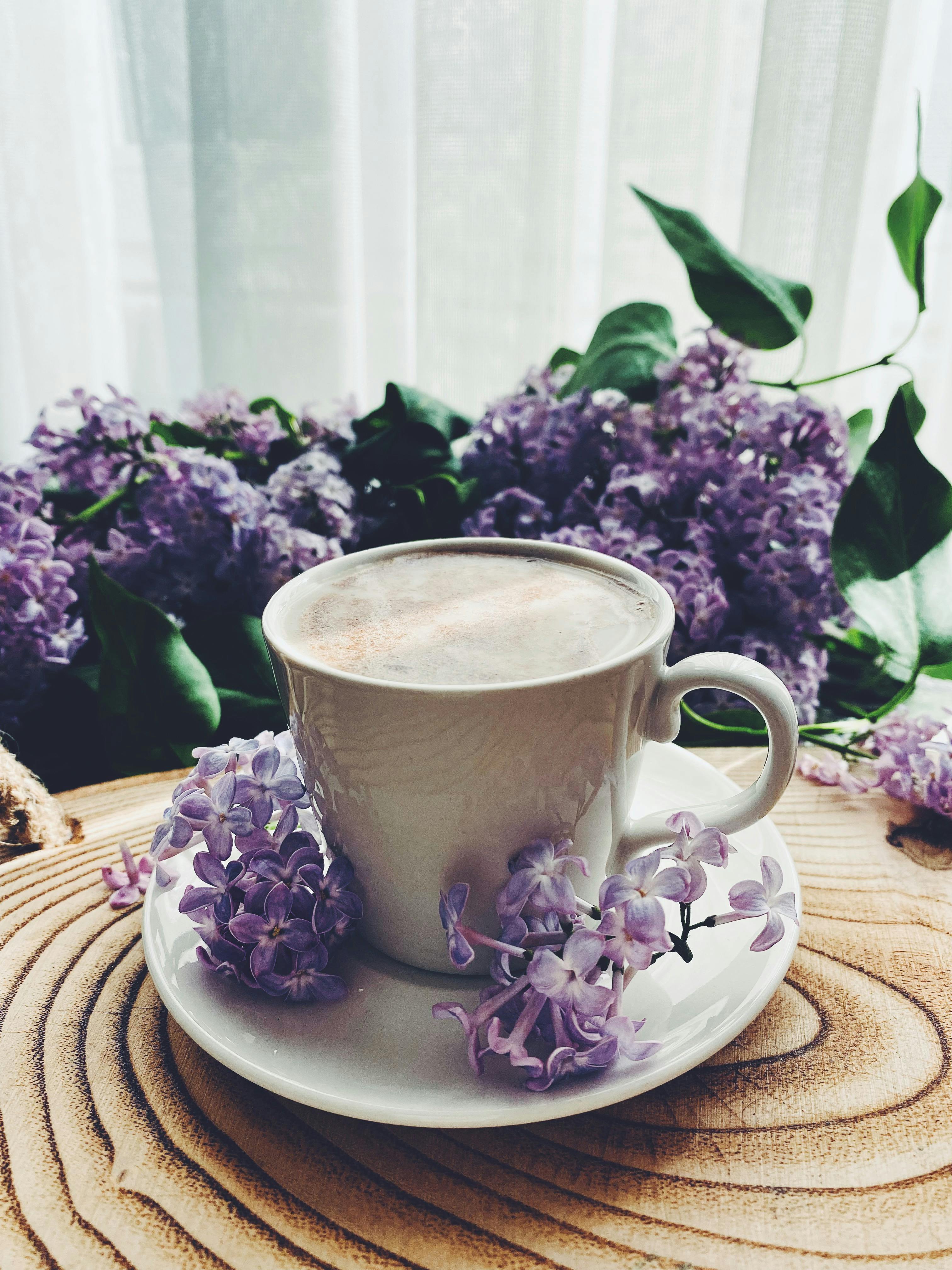 A serene cup of coffee surrounded by lilac blossoms on a rustic wooden table, perfect for a calming morning setting.