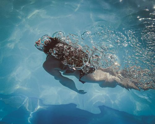 Free A woman swims underwater in a clear pool, releasing bubbles while enjoying a sunny swim. Stock Photo