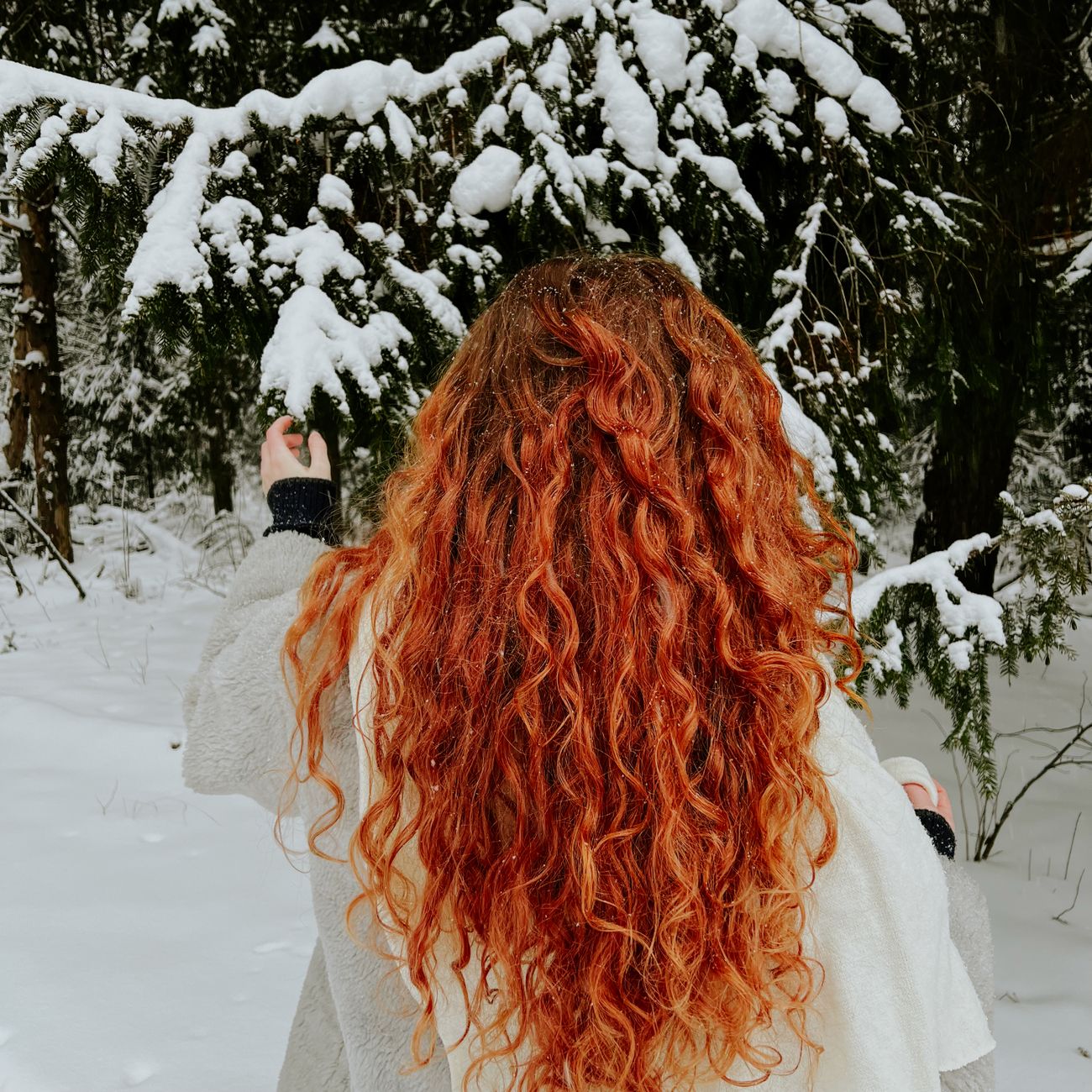 Redhead woman with curly hair in a snowy forest, capturing winter's beauty.