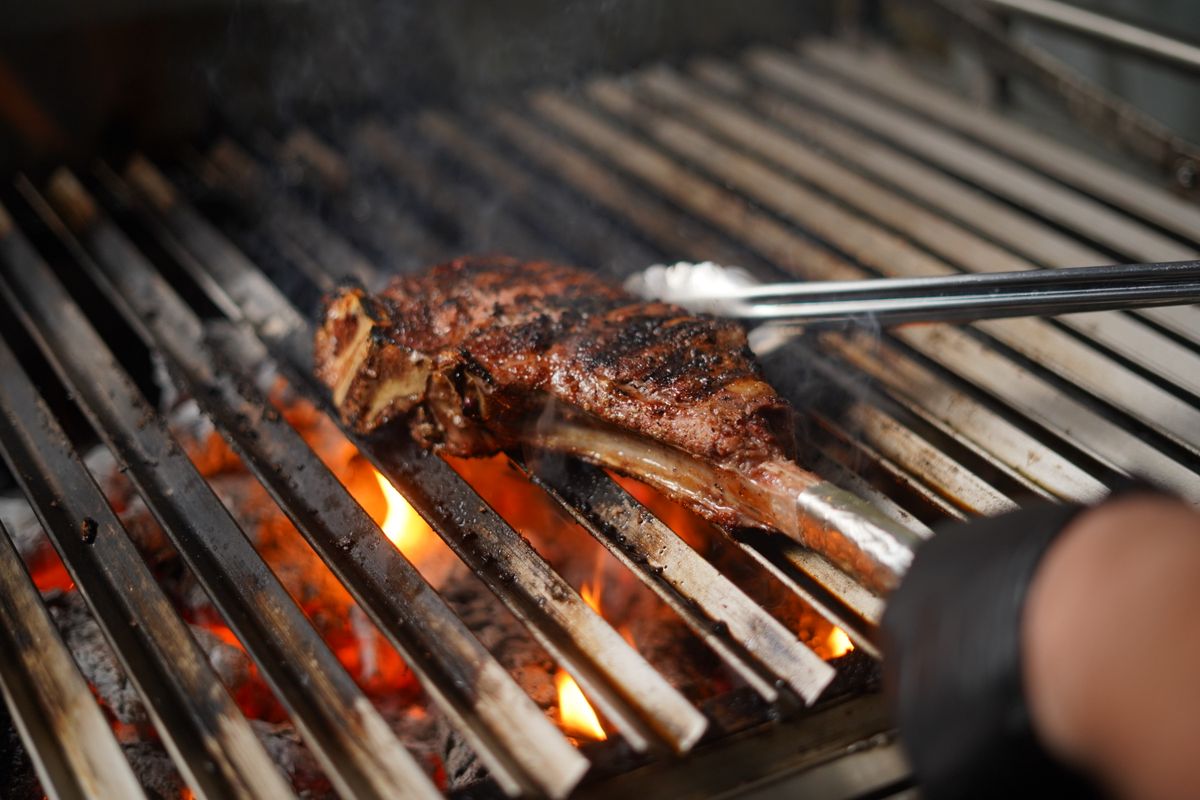 Bone-in steak turned with tongs over glowing charcoal on a grill