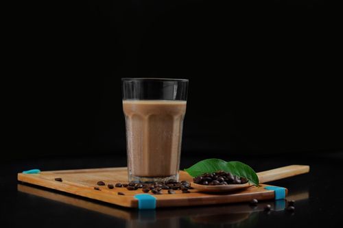 Free Refreshing iced coffee served on a wooden tray with scattered coffee beans and green leaf accent. Stock Photo