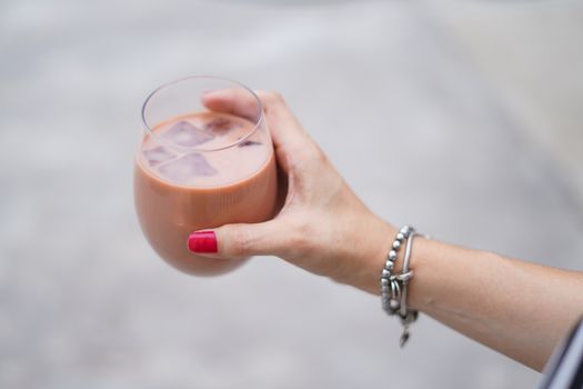 Close-up of a woman's hand holding a glass of iced coffee with bracelets, outdoors.
