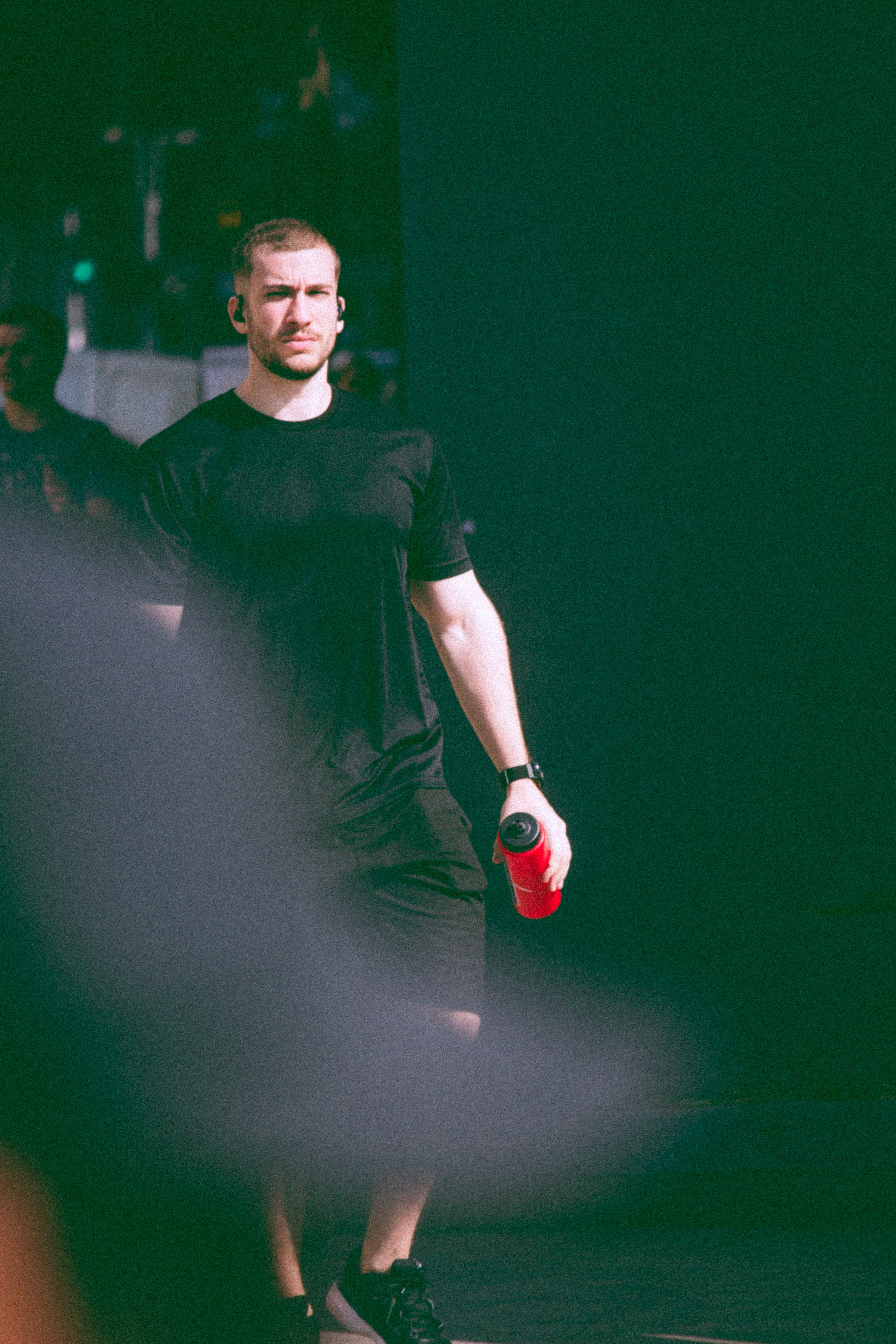 A fit man in black attire holding a red water bottle outdoors, exuding a sporty vibe.
