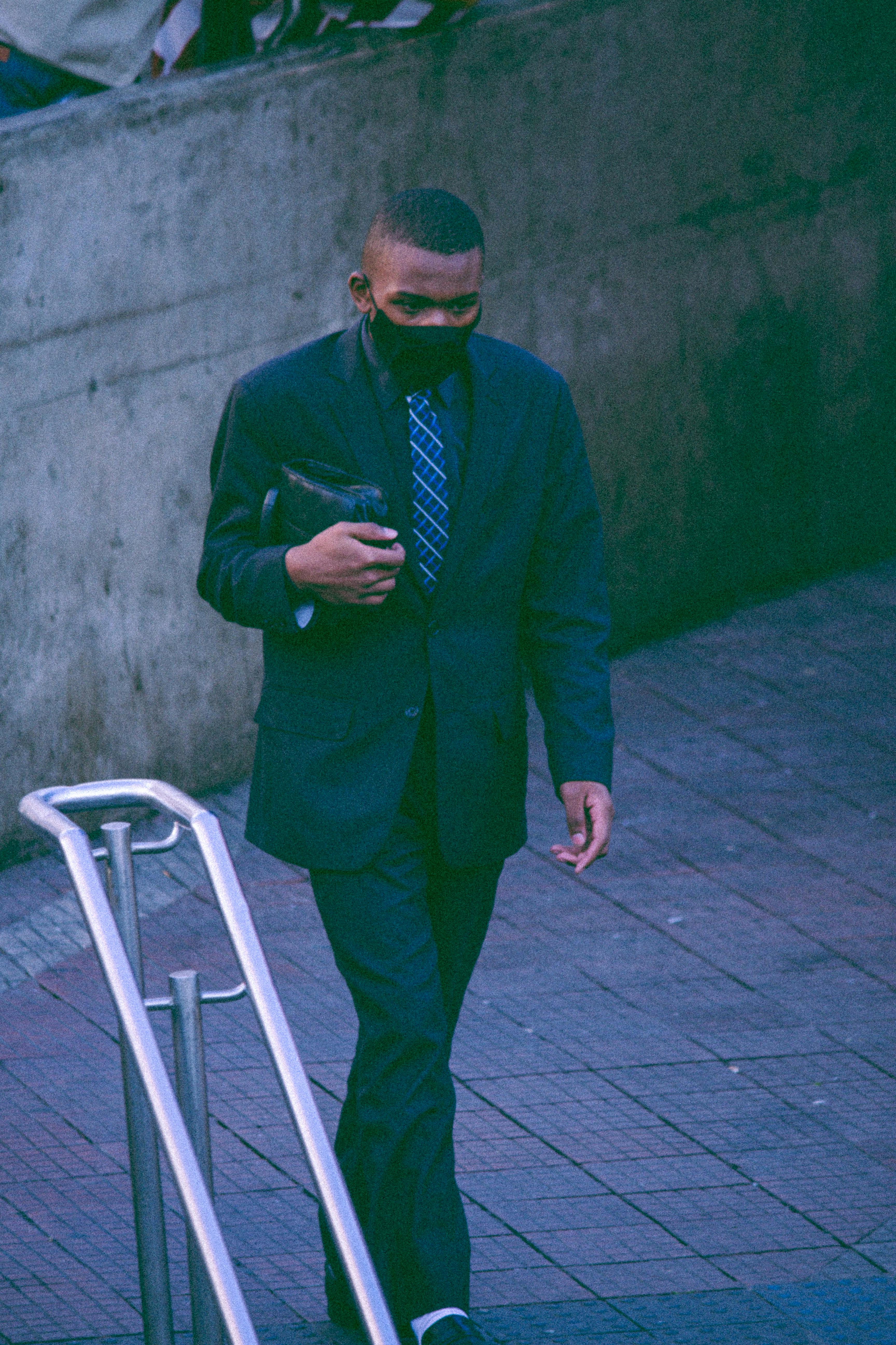 A professional man in a suit and mask walking outdoors. Perfect for business themes.