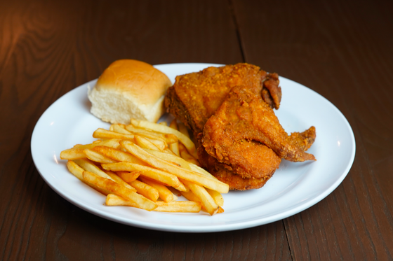 Crispy fried chicken breast quarter with wing, french fries and soft dinner roll on white plate