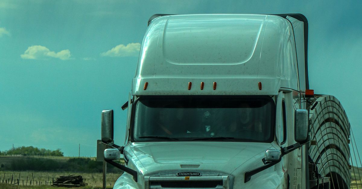 A white semi-truck travels on a highway under a cloudy, dramatic sky.