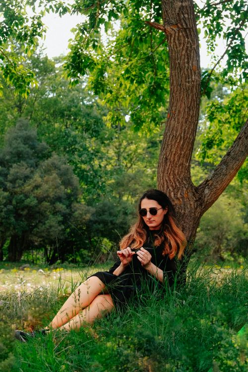 Free Woman sitting under a tree in countryside wearing sunglasses and black dress. Stock Photo