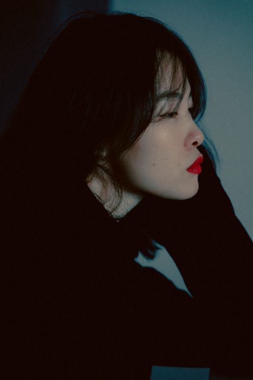Free Moody portrait of a young woman with red lipstick posing in a dark setting, wearing a sweater. Stock Photo