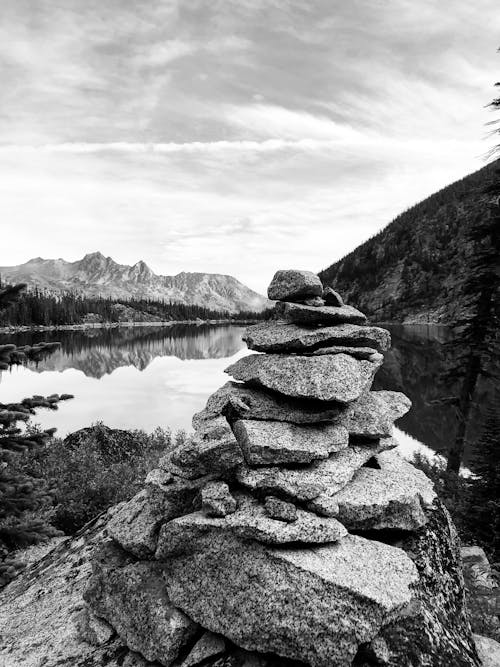 Black and White Photo of a Stack of Stones with a Lake and Mountains in the Background 