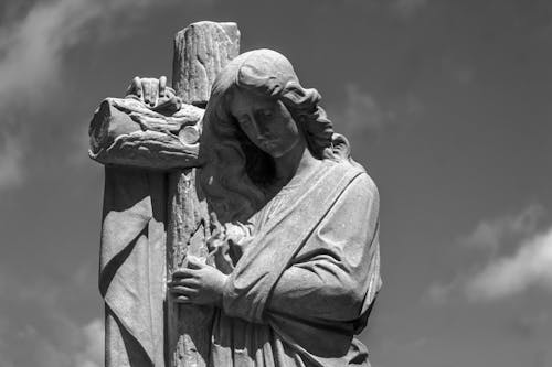 Grayscale Photo of a Cross and a Statue