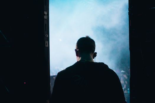 Back view of a DJ with headphones standing on stage in smoky atmosphere.