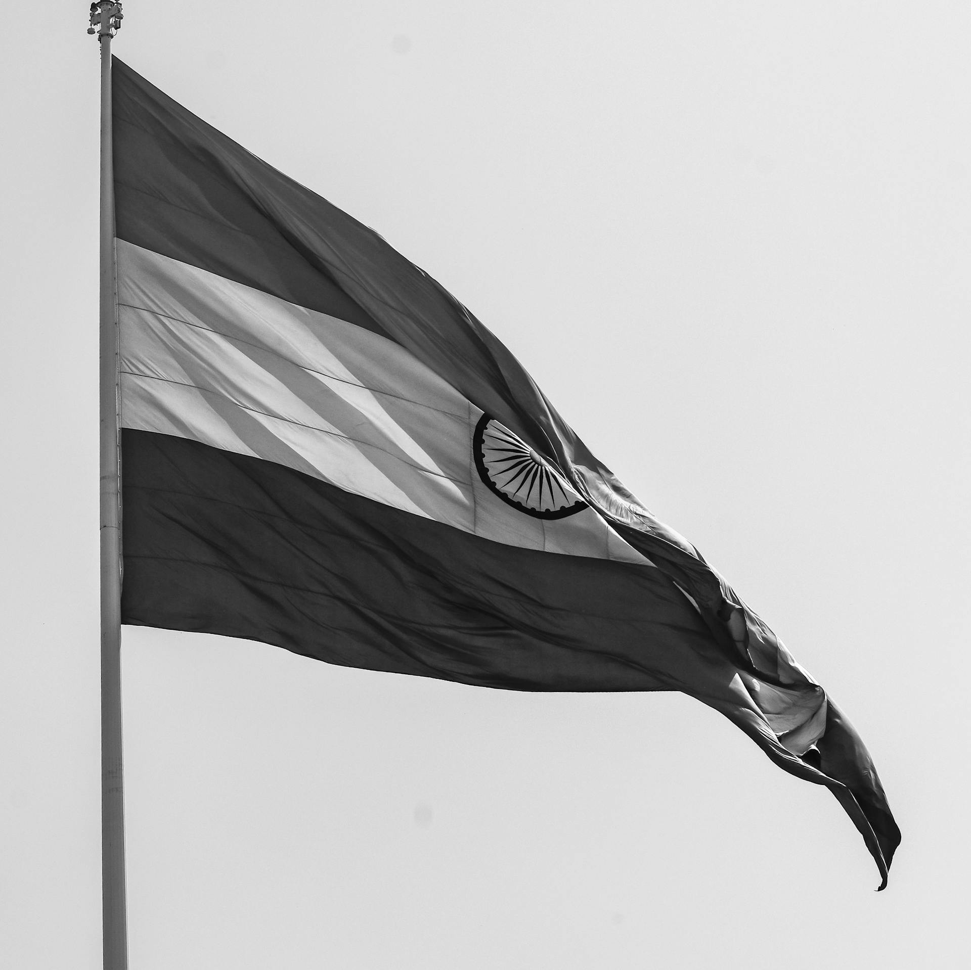 A black and white image of the Indian flag waving proudly against a clear sky.